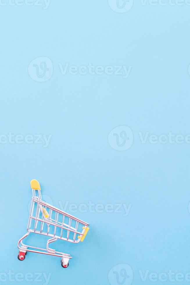 Abstract design element, annual sale, shopping season concept, mini yellow cart with colorful paper bag on pastel blue background, top view, flat lay photo