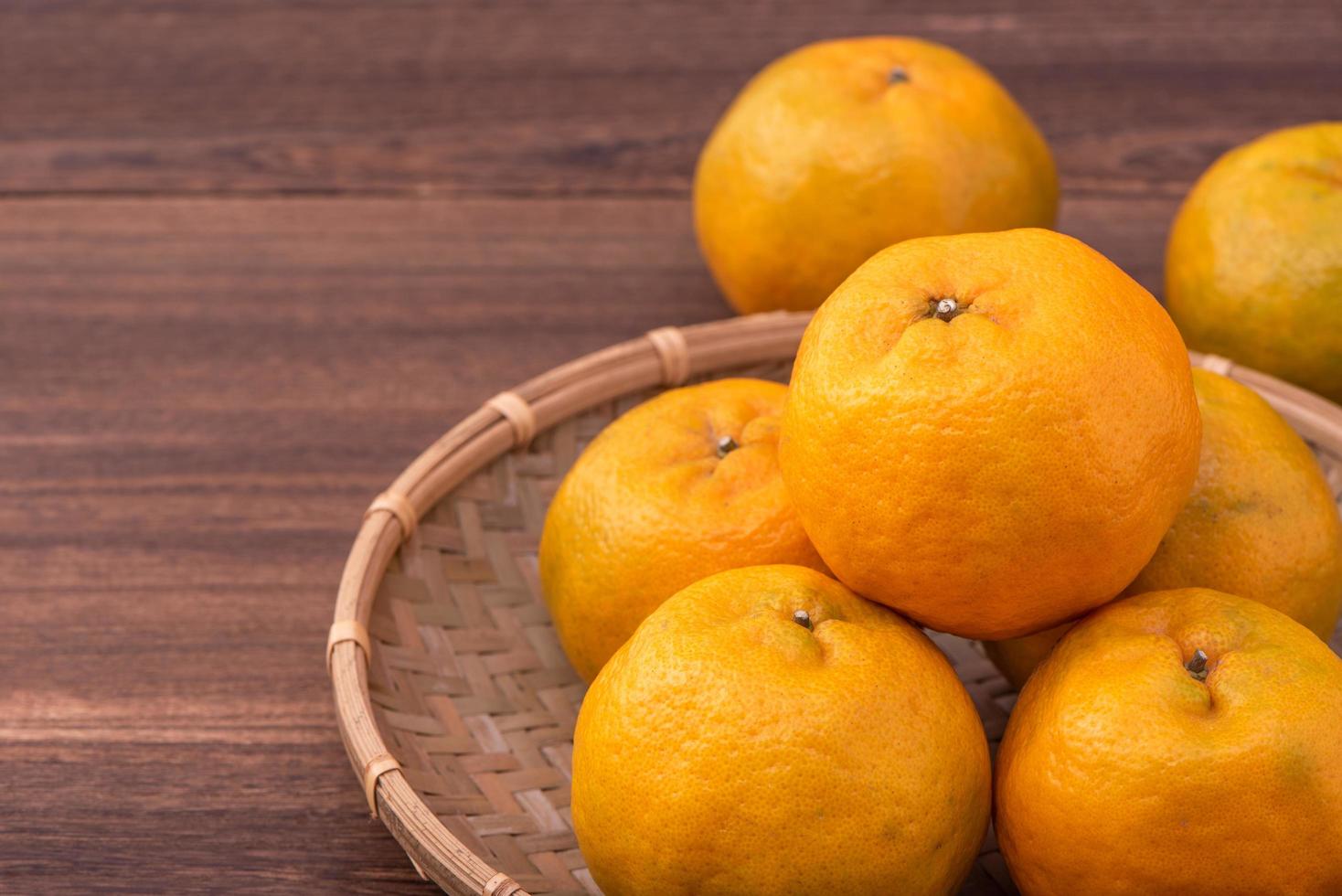 Fresh, beautiful orange color tangerine on bamboo sieve over dark wooden table. Seasonal, traditional fruit of Chinese lunar new year, close up. photo