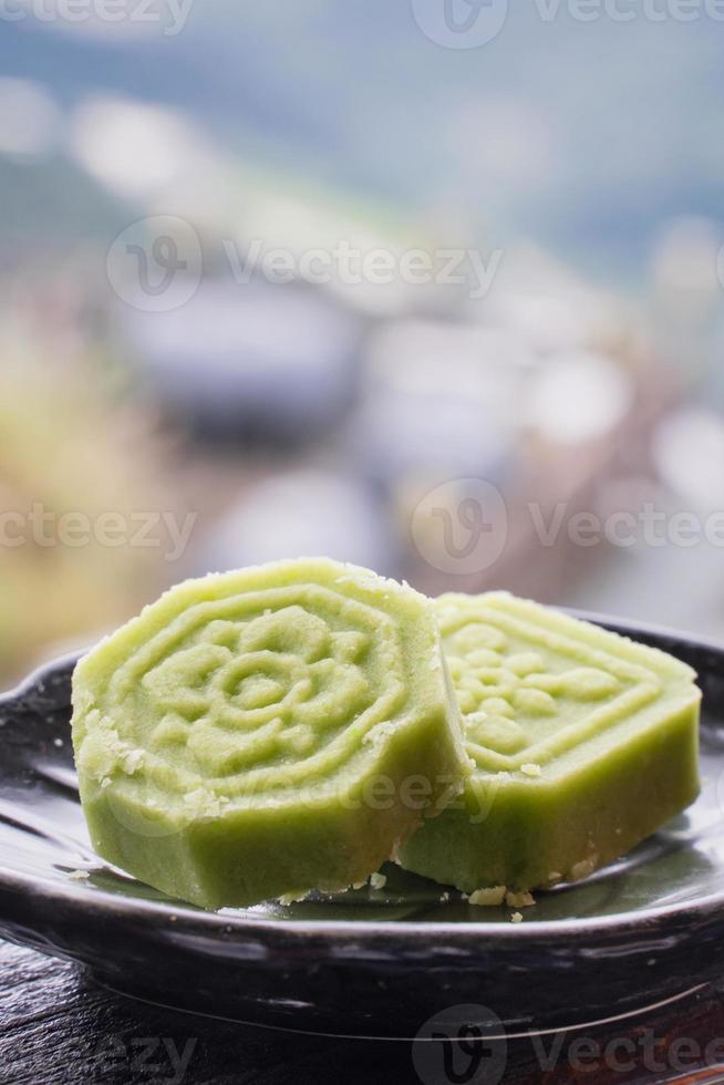 Delicious green mung bean cake with black tea plate on wooden railing of a teahouse in Taiwan with beautiful landscape in background, close up. photo