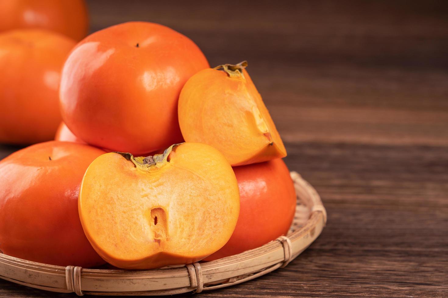 Fresh, beautiful orange color persimmon kaki on bamboo sieve over dark wooden table. Seasonal, traditional fruit of Chinese lunar new year, close up. photo