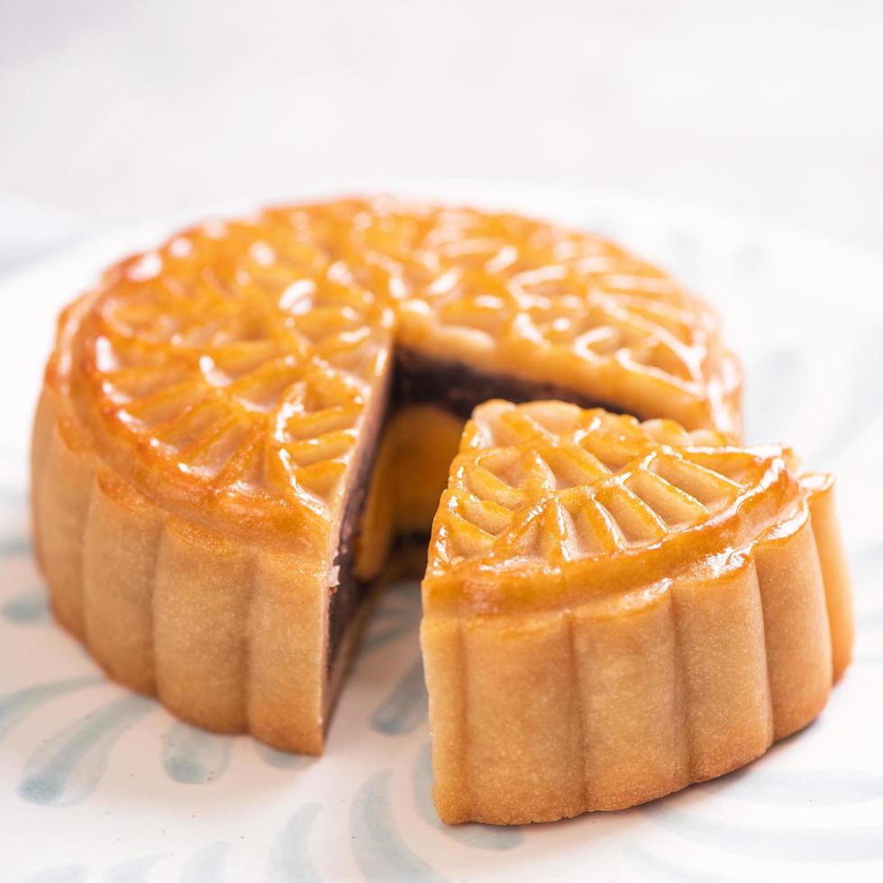 Mid-Autumn Festival traditional food concept - Beautiful cut moon cake on blue pattern plate on white background with flower, close up, copy space photo