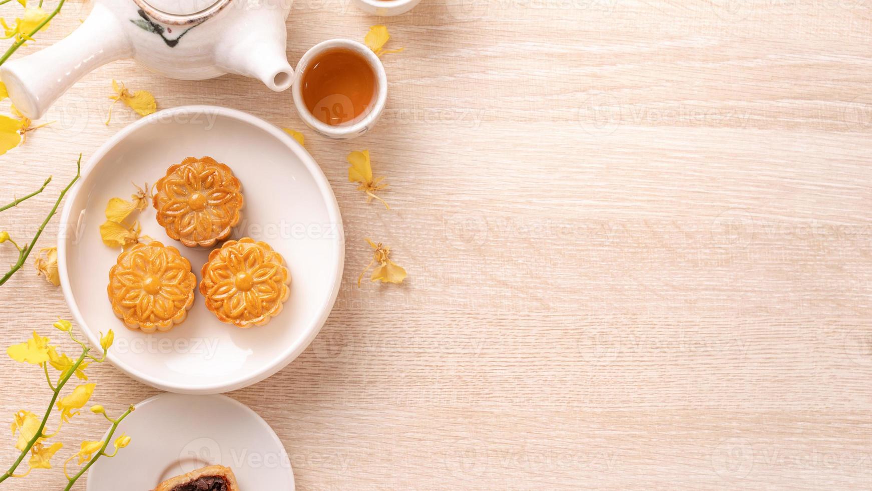 sabroso pastel de luna para el festival de mediados de otoño en una mesa de madera brillante, concepto de té festivo decorado con flores amarillas, vista superior, puesta plana. foto