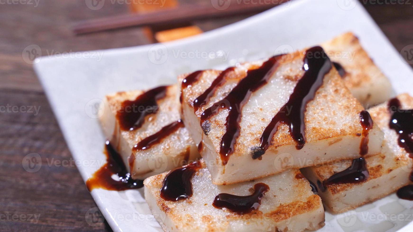 Pouring black soy sauce on ready-to-eat delicious turnip cake, Chinese traditional local dish radish cake in restaurant, close up, copy space. photo