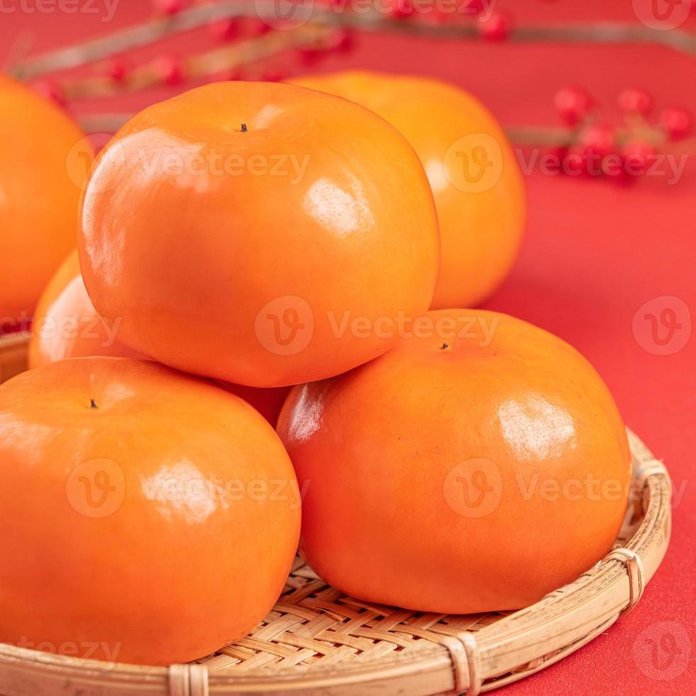 Fresh beautiful sliced sweet persimmon kaki isolated on red table background and bamboo sieve, Chinese lunar new year design concept, close up. photo