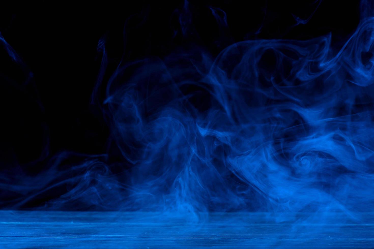 Conceptual image of blue smoke isolated on dark black background and wooden table. photo