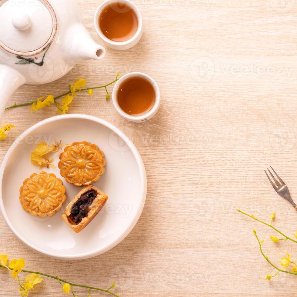 Tasty moon cake for Mid-Autumn festival on bright wooden table, concept of festive afternoon tea decorated with yellow flowers, top view, flat lay. photo