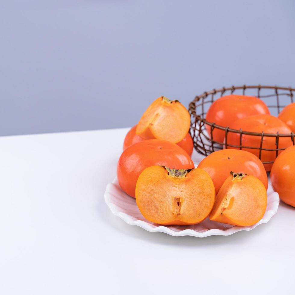 Fresh beautiful sliced sweet persimmon kaki isolated on white kitchen table with gray blue background, Chinese lunar new year design concept, close up. photo