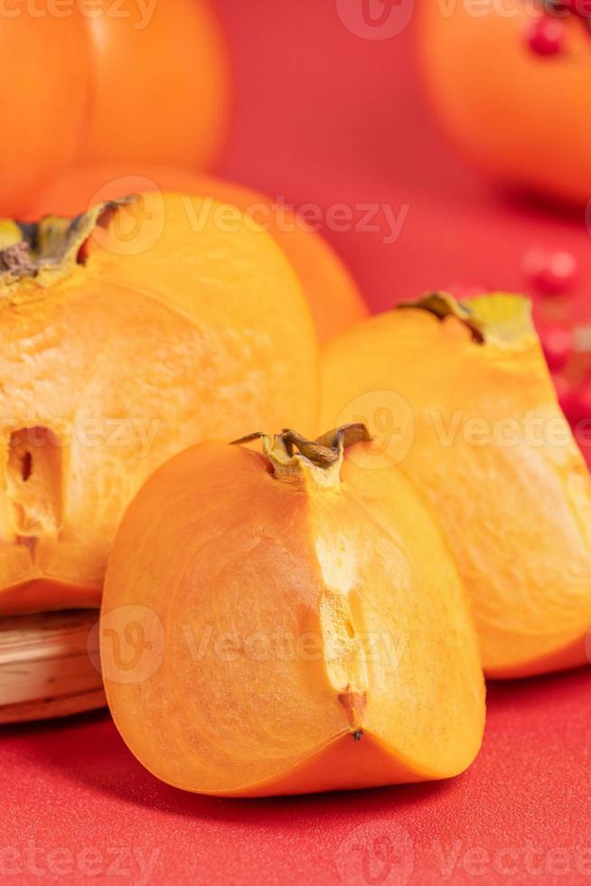 Fresh beautiful sliced sweet persimmon kaki isolated on red table background and bamboo sieve, Chinese lunar new year design concept, close up. photo
