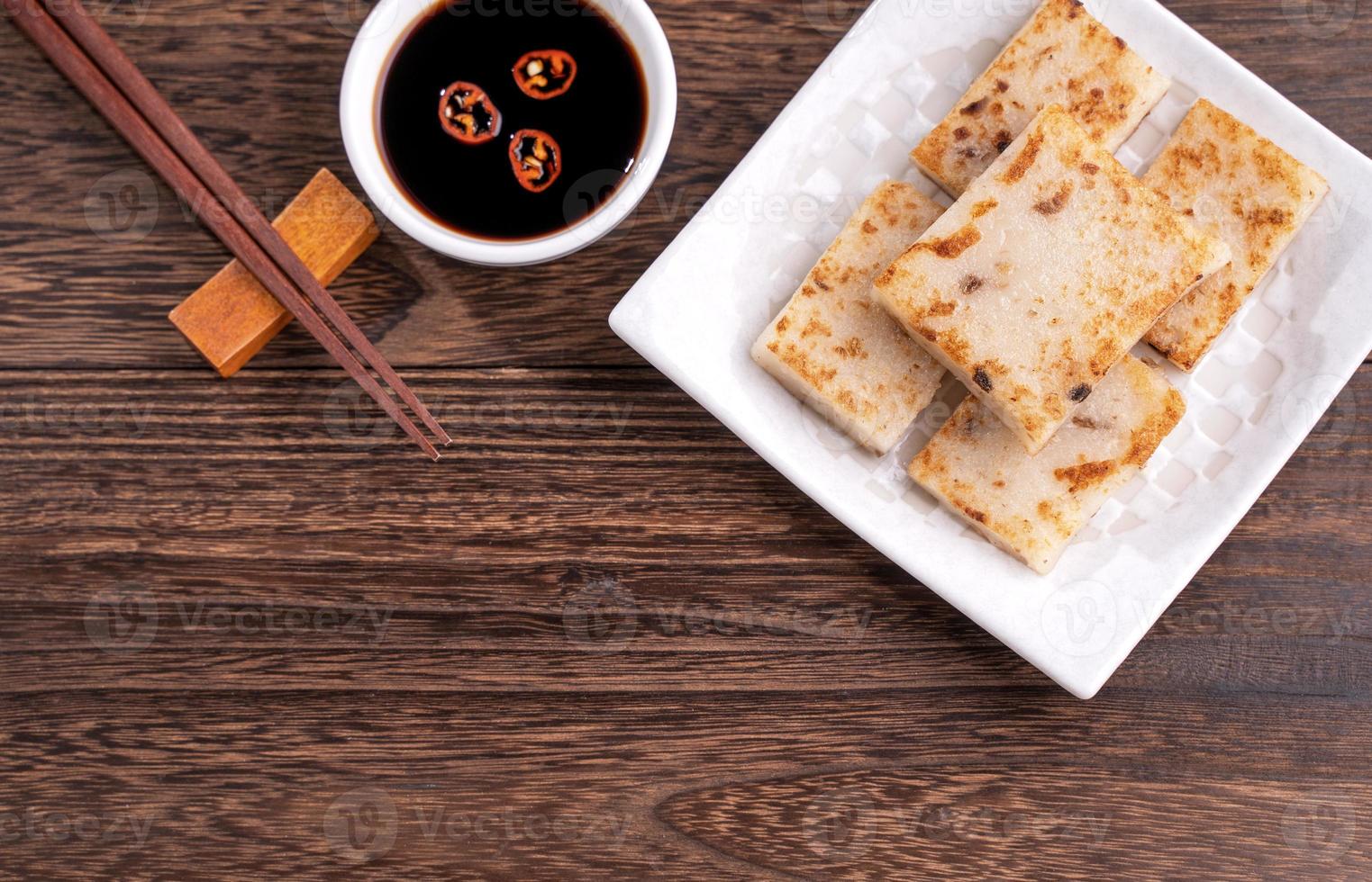 Delicious turnip cake, Chinese traditional local radish cake in restaurant with soy sauce and chopsticks, close up, copy space, top view, flat lay. photo