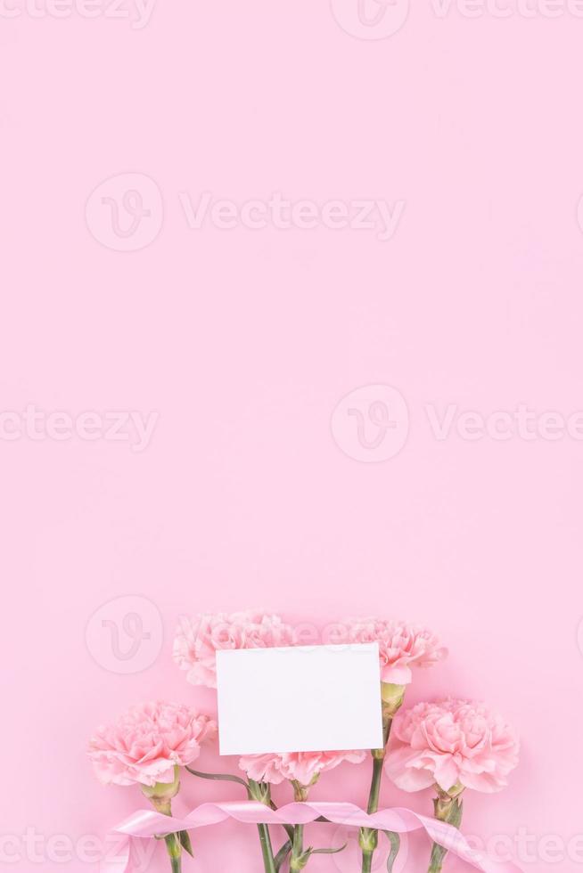 Beautiful, fresh elegant carnation flower bouquet with white greeting thanks gift card isolated on bright pink color background, top view, flat lay concept. photo