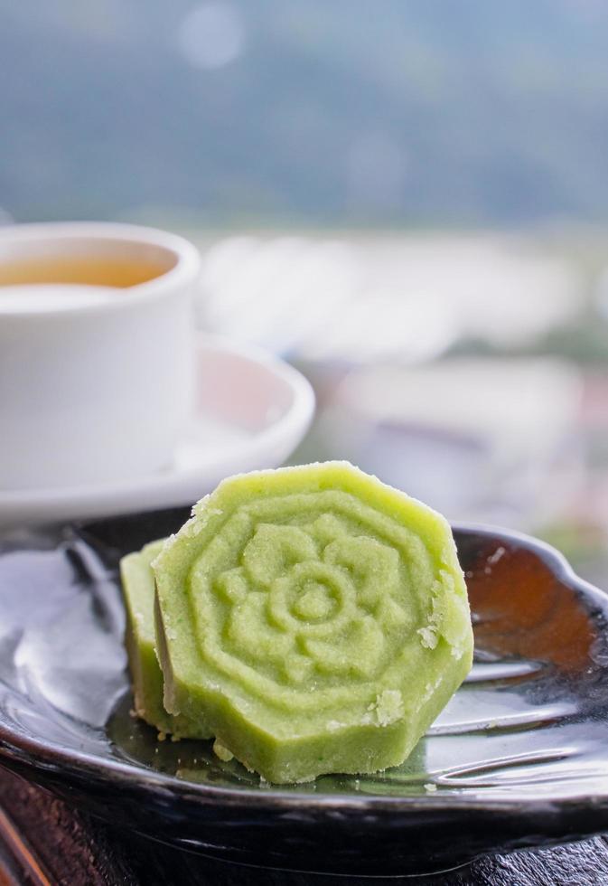 Delicioso pastel de frijol mungo verde con plato de té negro en una barandilla de madera de una casa de té en taiwán con un hermoso paisaje de fondo, de cerca. foto