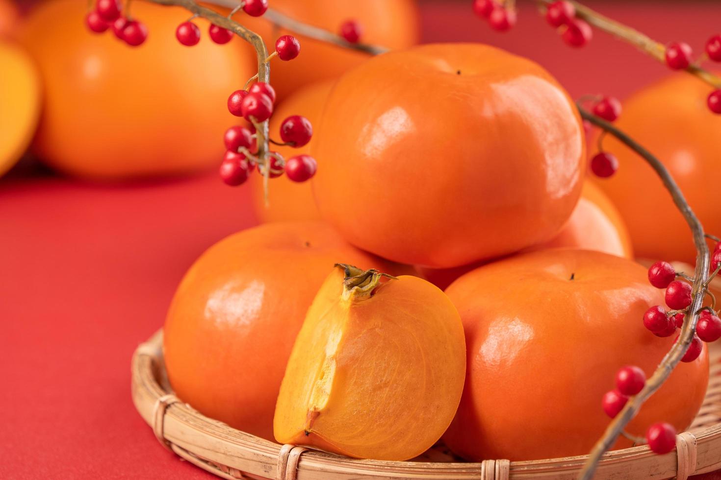 Fresh beautiful sliced sweet persimmon kaki isolated on red table background and bamboo sieve, Chinese lunar new year design concept, close up. photo