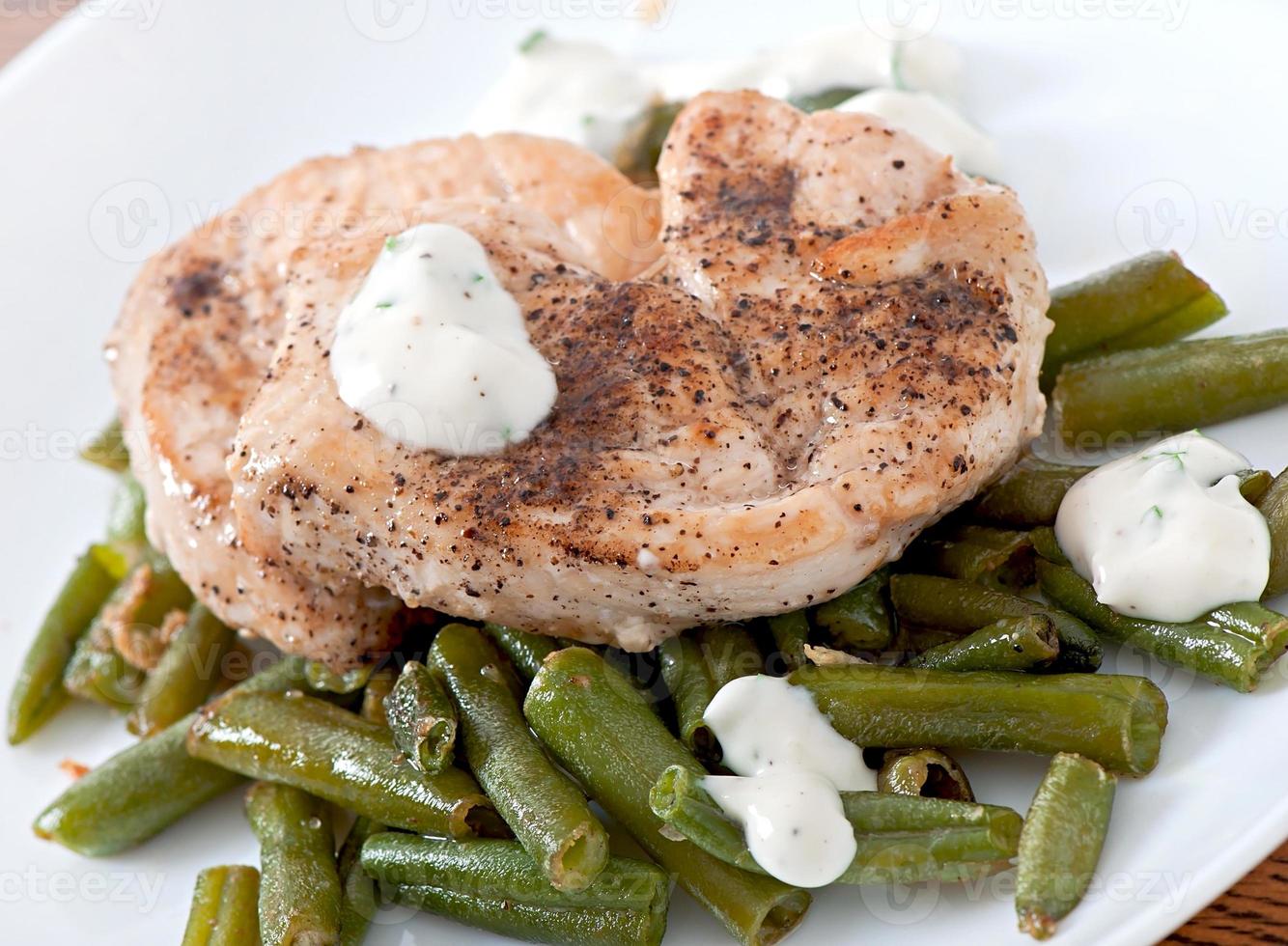 Grilled chicken breast with green beans and sauce on a white plate. photo