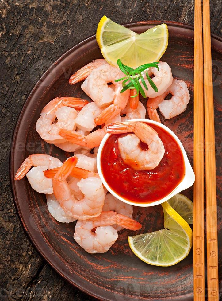tails of shrimps with fresh lemon and rosemary in plate on wooden old background photo