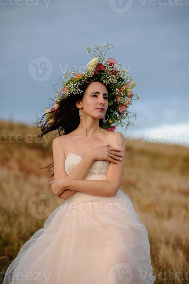 the bride in a beautiful blue dress with a deep neckline at the back with a wreath on her head of white flowers stands on a background of mountains and lakes photo