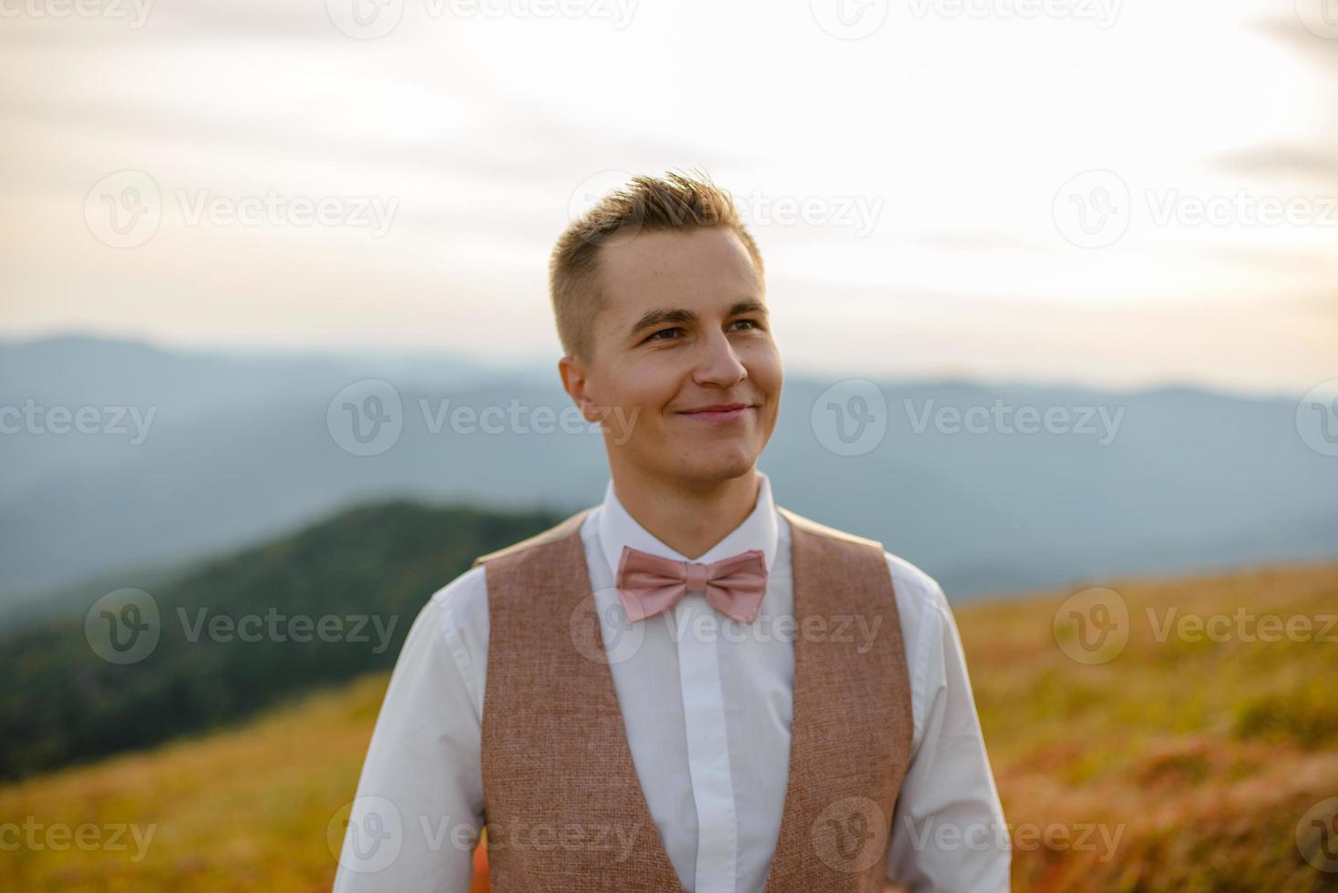 back of a young man in costume standing on a mountain at sunset. The groom or businessman looks from the top. photo