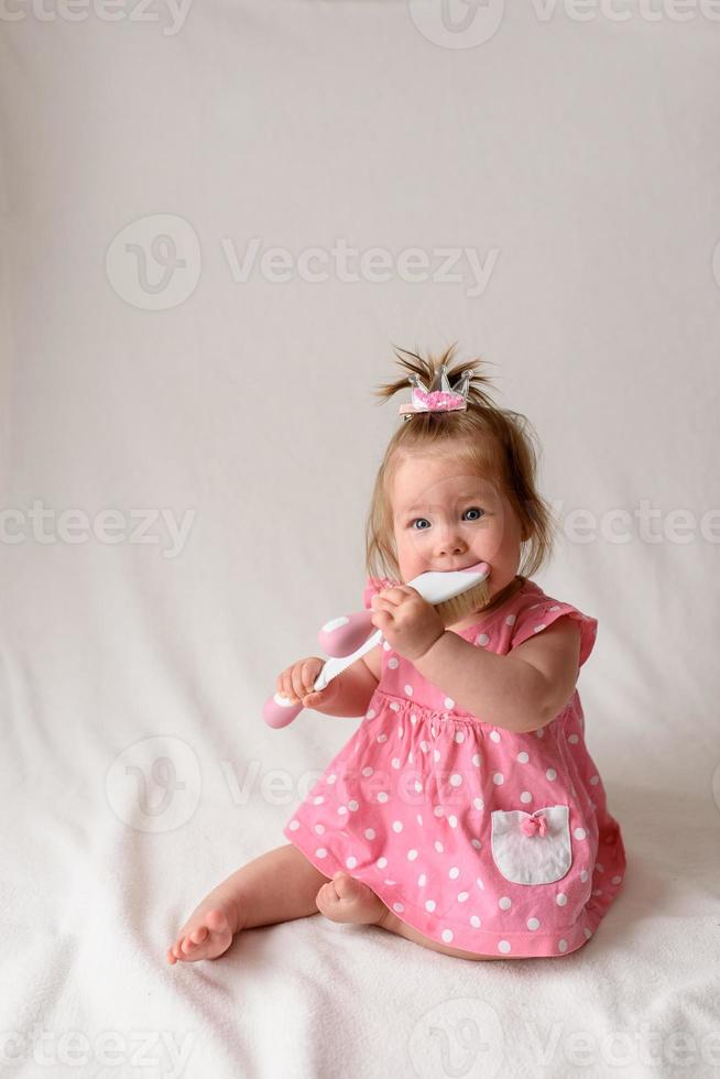 niña de 6 meses con un peine en la mano sobre un fondo blanco. foto