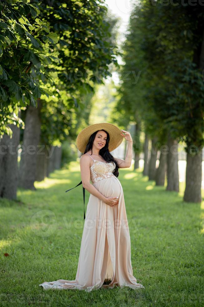 mujer embarazada con un sombrero posando con un vestido sobre un fondo de árboles verdes. foto