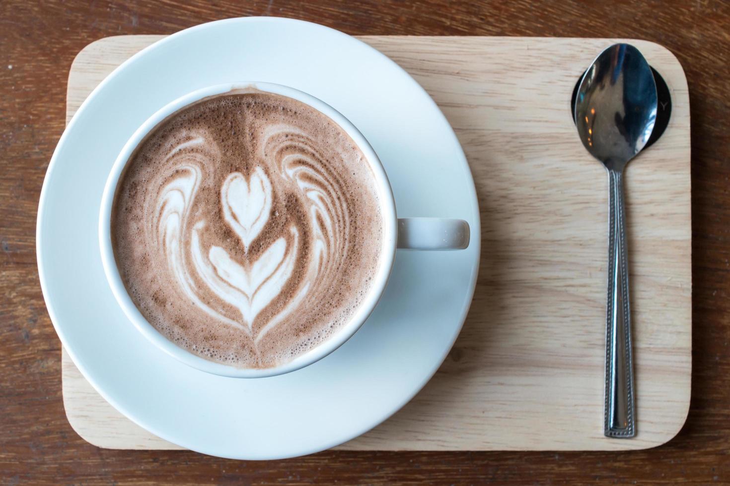 Close-up shot of a cup of hot chocolate with latte art on the surface serving on wooden table. photo