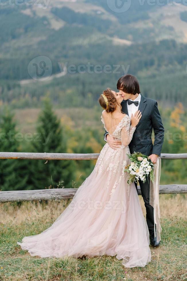 La novia y el novio jóvenes y elegantes se paran en un bote en el fondo del cielo nublado, el mar y las montañas de montenegro. foto