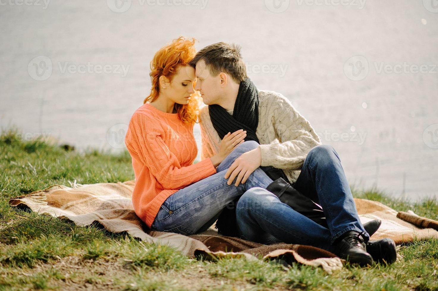 joven pareja enamorada relajándose en el lago de otoño. hombre y mujer felices disfrutando de la naturaleza y abrazándose. relajarse al aire libre foto