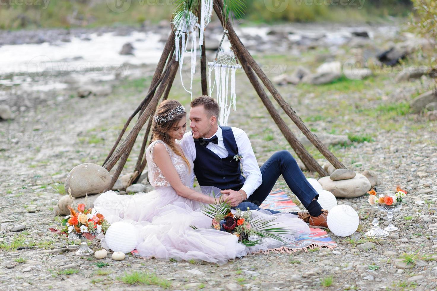 una atractiva pareja de recién casados, un momento feliz y alegre. un hombre y una mujer se afeitan y se besan con ropa de fiesta. ceremonia de boda de estilo bohemio en el bosque al aire libre. foto