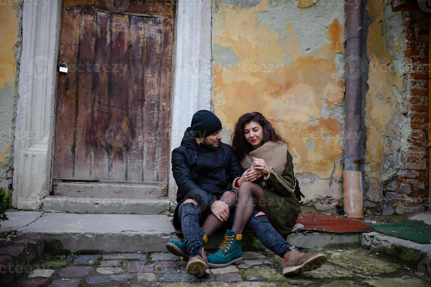 A young romantic couple wearing warm clothes outdoor at Christmas time, sitting on a bench in evening street decorated with beautiful lights. photo