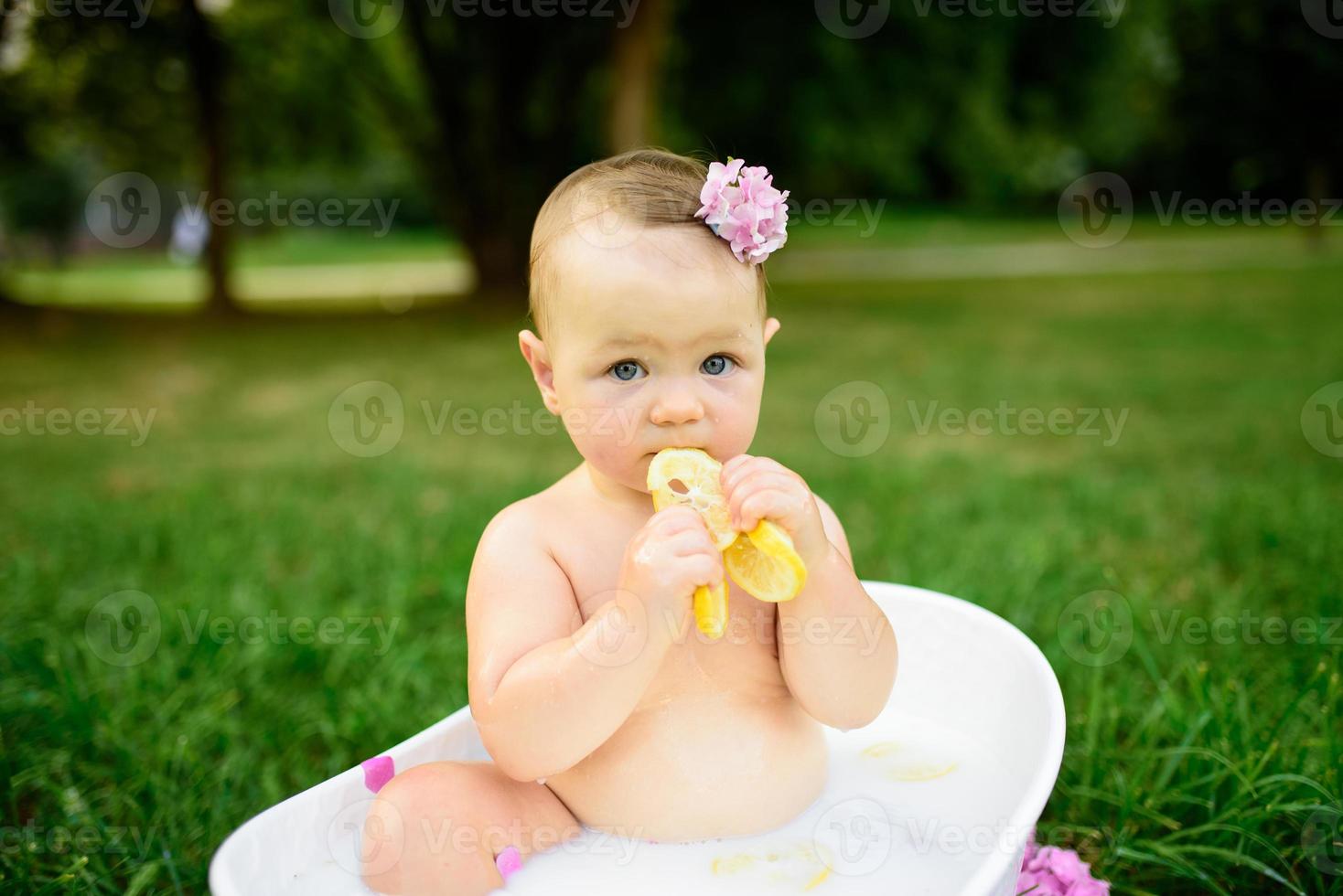 Little girl bathes in a milk bath in the park. The girl is having fun in the summer. photo