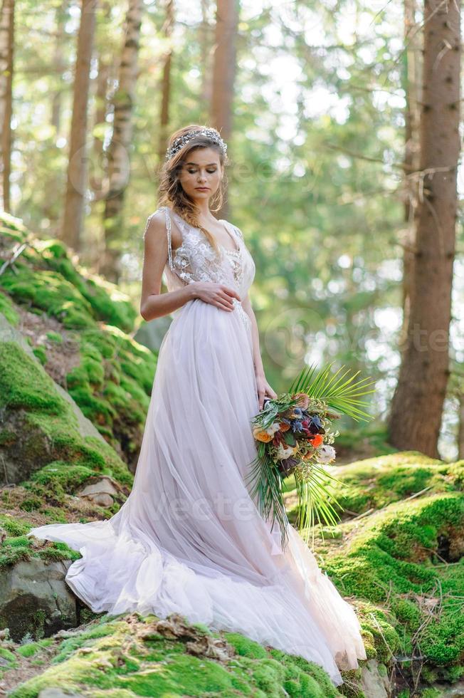 Happy bride in a pink wedding dress. The girl holds a wedding bouquet in her hands. Boho style wedding ceremony in the forest. photo