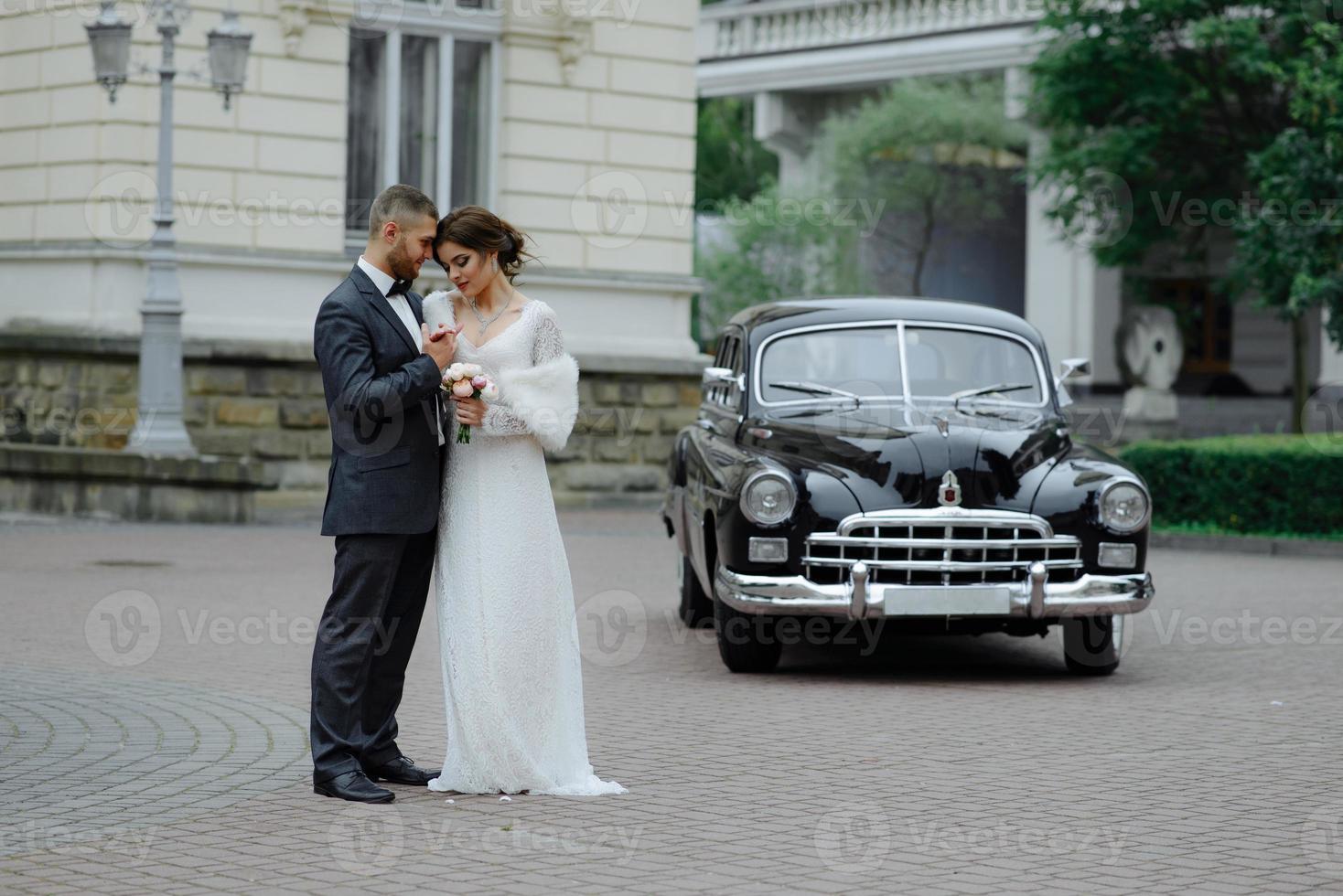 Happy luxury wedding couple kissing and embracing near retro with bouquet car in autumn photo