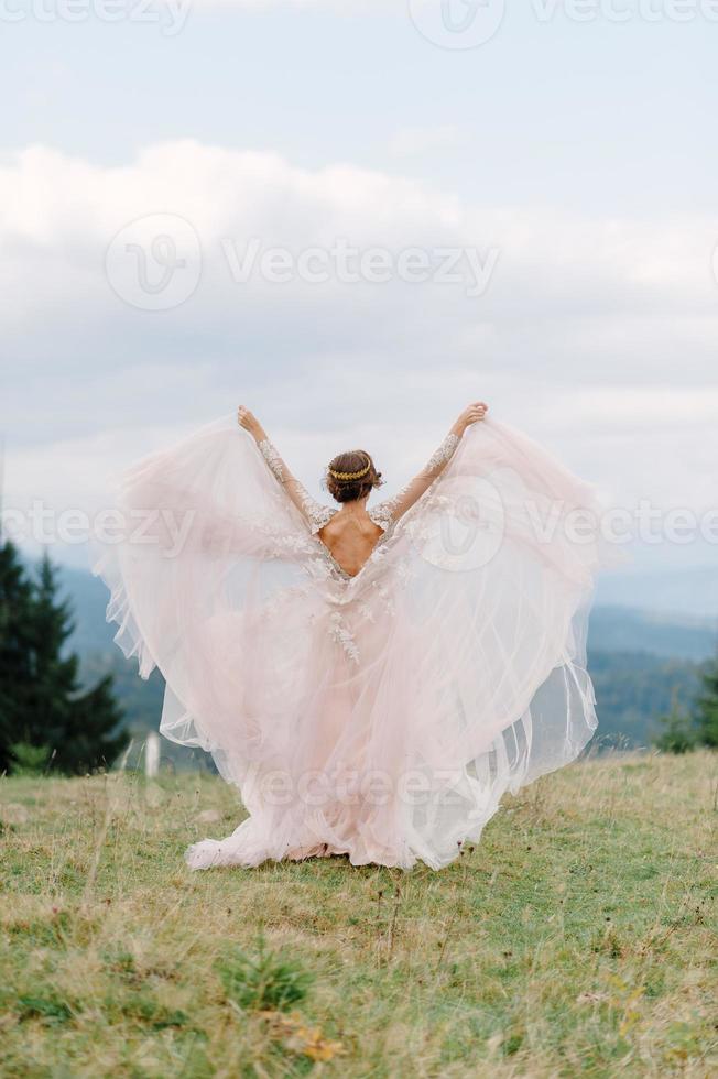 whirling bride holding veil skirt of wedding dress at pine forest photo
