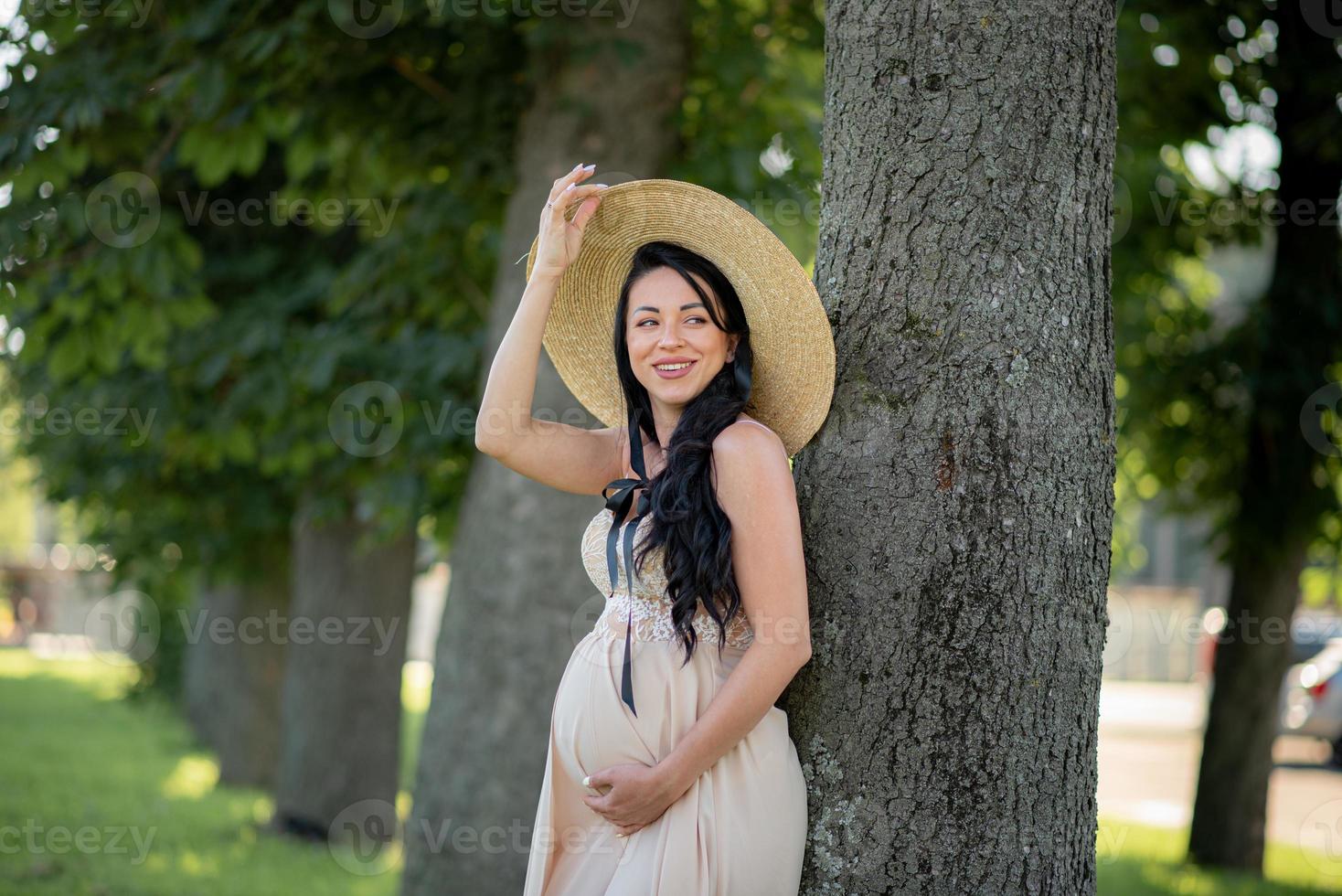Pregnant woman in a hat posing in a dress on a background of green trees. photo