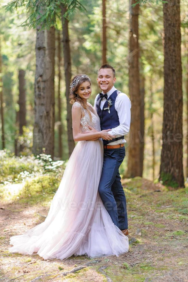 una atractiva pareja de recién casados, un momento feliz y alegre. un hombre y una mujer se afeitan y se besan con ropa de fiesta. ceremonia de boda de estilo bohemio en el bosque al aire libre. foto