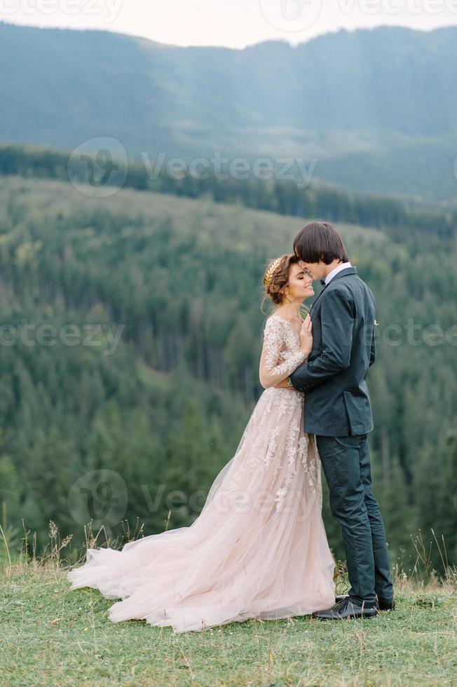 La novia y el novio jóvenes y elegantes se paran en un bote en el fondo del cielo nublado, el mar y las montañas de montenegro. foto