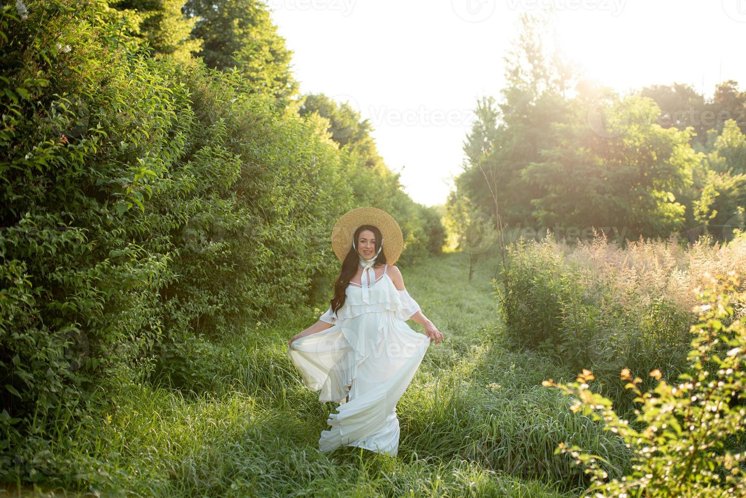 Pregnant woman in a hat posing in a dress on a background of green trees. photo