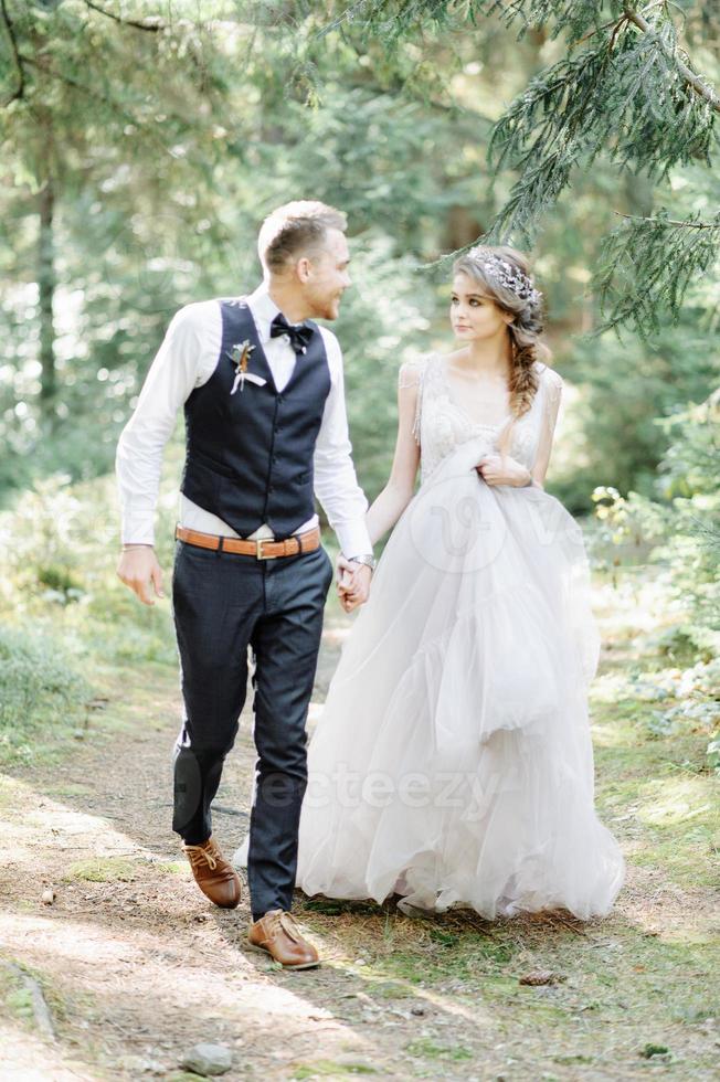 Attractive couple newlyweds, happy and joyful moment. Man and woman in festive clothes sit on the stones near the wedding decoration in boho style. Ceremony outdoors. photo