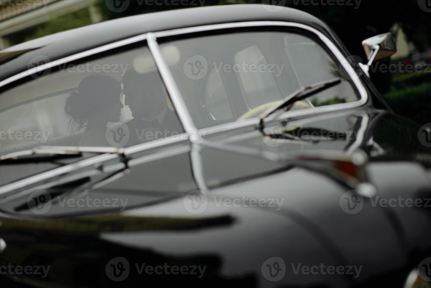 Beautiful happy young bride and groom looking from retro auto photo
