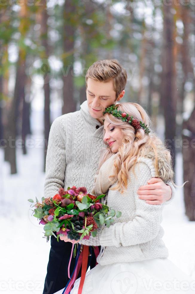 la novia y el novio están sentados en el tronco en el bosque de invierno. de cerca. ceremonia de boda de invierno. foto