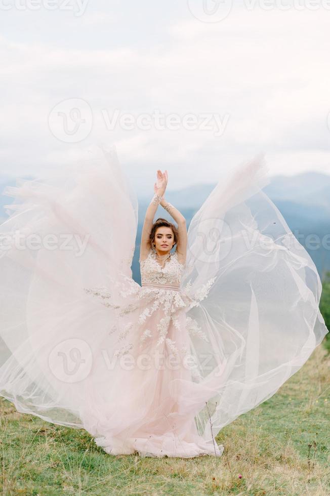 whirling bride holding veil skirt of wedding dress at pine forest photo