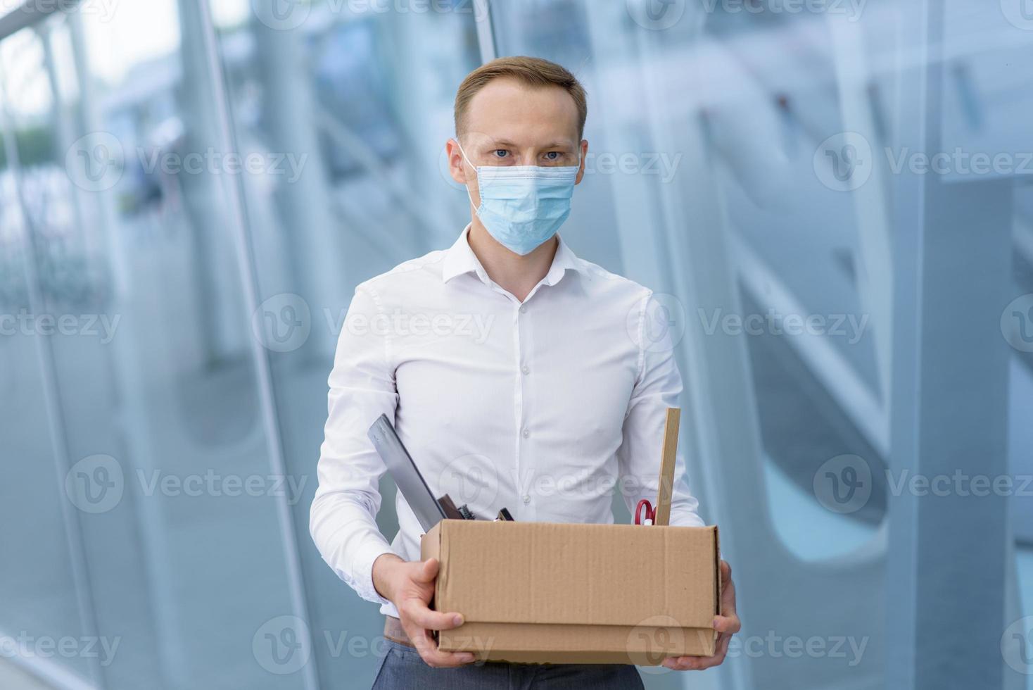 The fired office worker fell to his knees and covered his face due to stress. In front of him is a cardboard box with stationery. The man is unhappy due to a reduction in the robot. photo