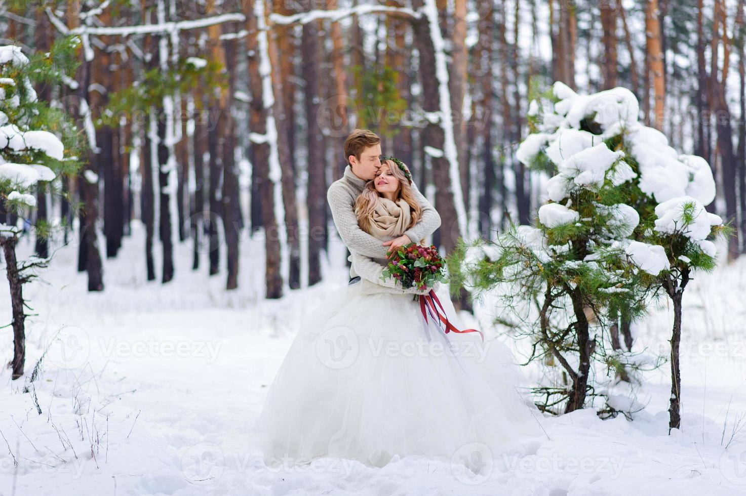 Bride and groom are sitting on the log in the winter forest. Close-up. Winter wedding ceremony. photo