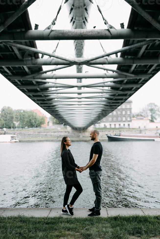 Young couple in love standing on the mountain hanging bridge hugging looking at each other smiling photo