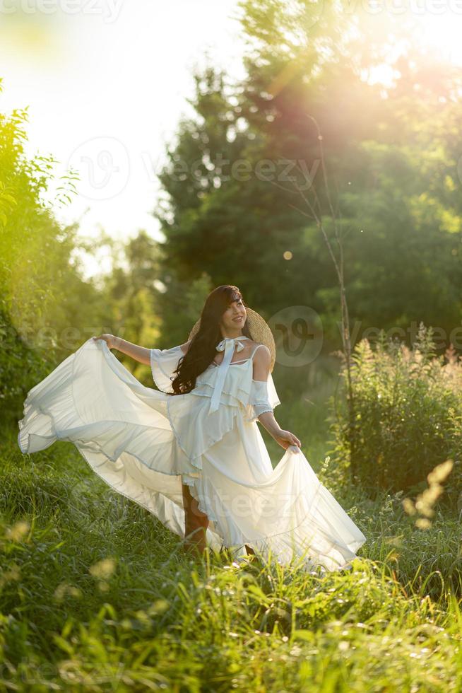 Pregnant woman in a hat posing in a dress on a background of green trees. photo