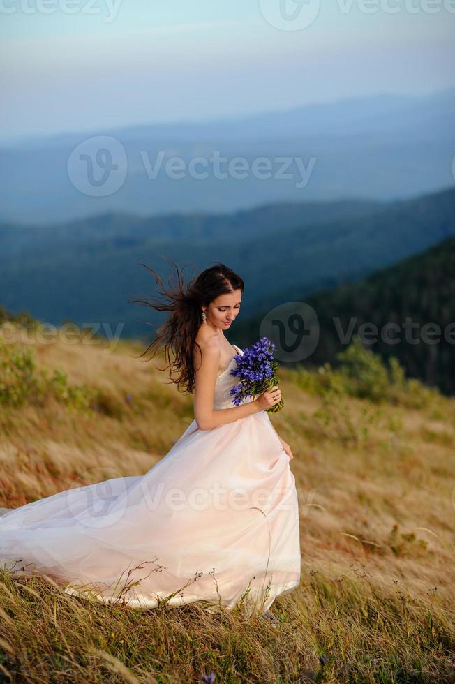 the bride in a beautiful blue dress with a deep neckline at the back with a wreath on her head of white flowers stands on a background of mountains and lakes photo