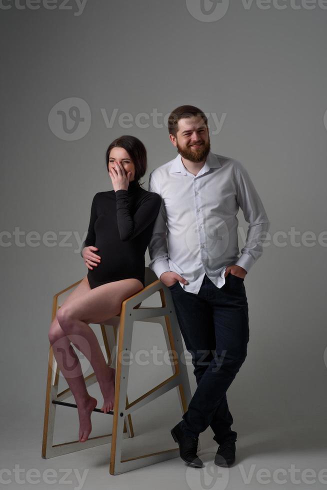 A pregnant woman and her husband are hugging on a gray background. Couple expecting a baby. photo