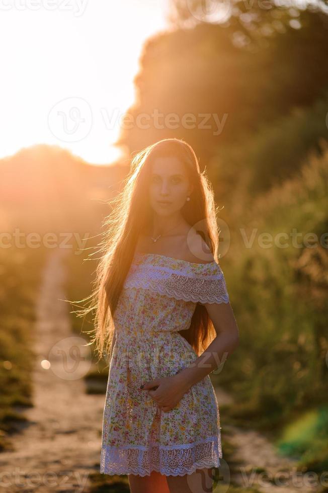 Portrait of a young beautiful girl in a sundress. Summer photo session in the park at sunset. A girl sits under a tree in the shade.