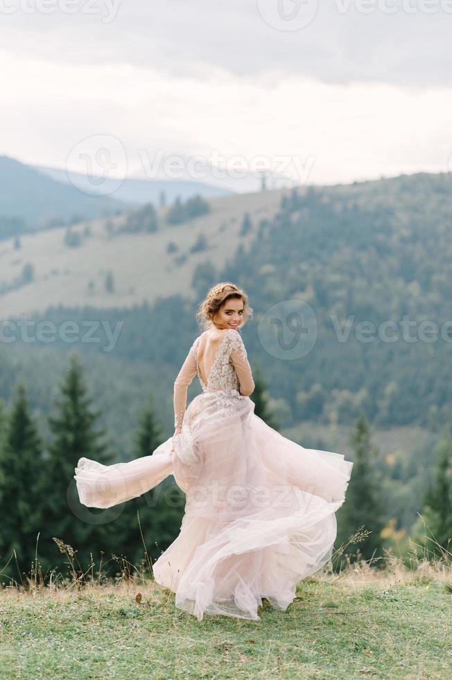 whirling bride holding veil skirt of wedding dress at pine forest photo