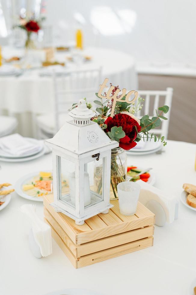 Round dinner tables covered with blue cloth stand in a white wedding pavilion photo