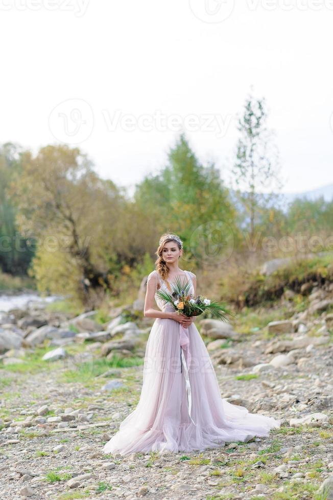 Happy bride in a pink wedding dress. The girl holds a wedding bouquet in her hands. Boho style wedding ceremony in the forest. photo