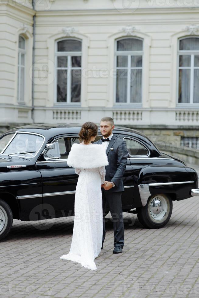 Happy luxury wedding couple kissing and embracing near retro with bouquet car in autumn photo